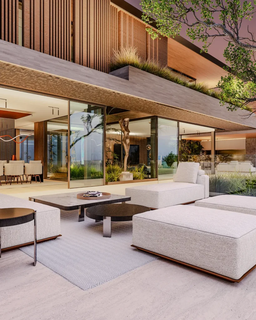 Villa Sehlangu – outdoor lounge terrace with cream upholstered seating, dark wood coffee tables, and a bronze figurative sculpture framed by glass doors into the open-plan living area at dusk.